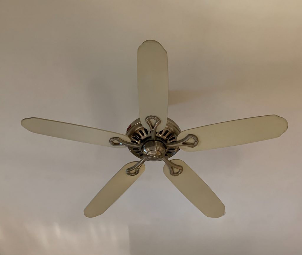 A still, dirty beige ceiling fan against a beige ceiling