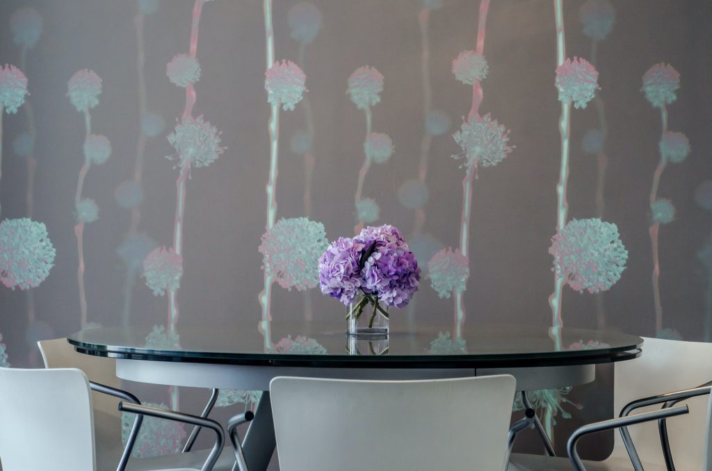 A dining room with a round dining table set and a lavender wall with pink and blue flowers painted