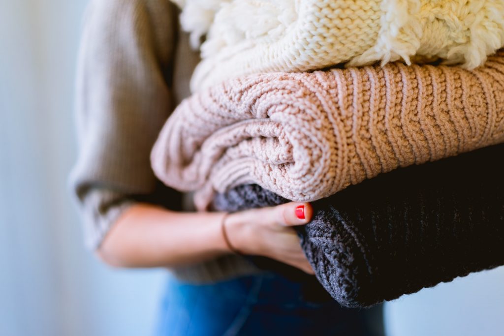A woman holding knitted sweaters
