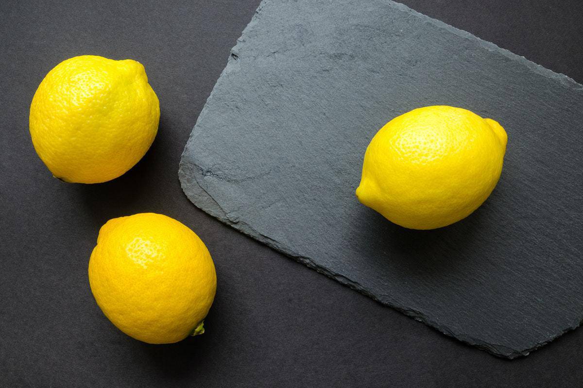 three lemons on a grey table and a slate cutting board