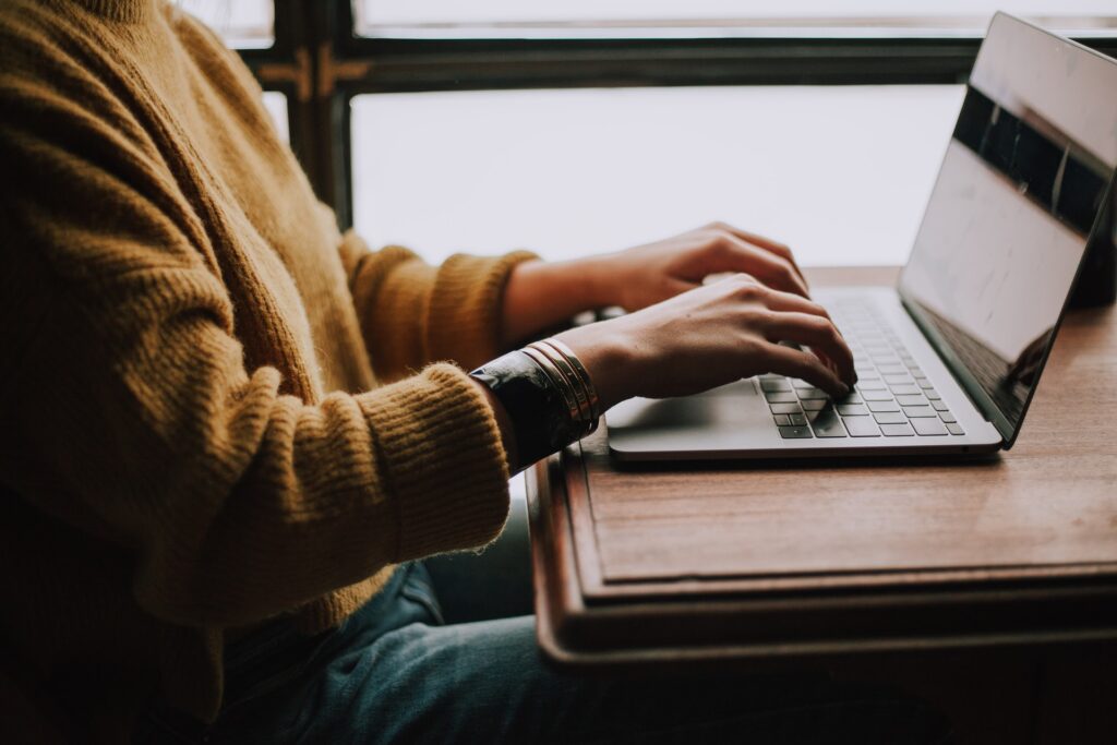 a woman in a mustard sweater typing on a laptop