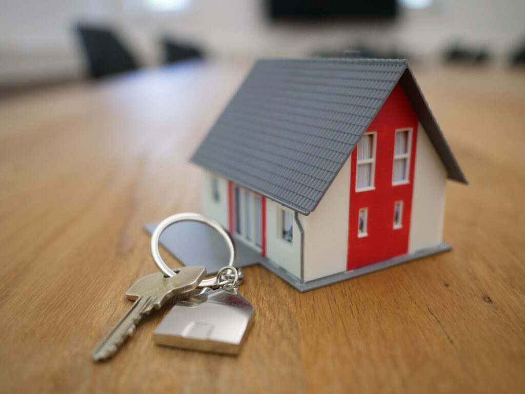 a toy plastic house on a table with house keys next to it