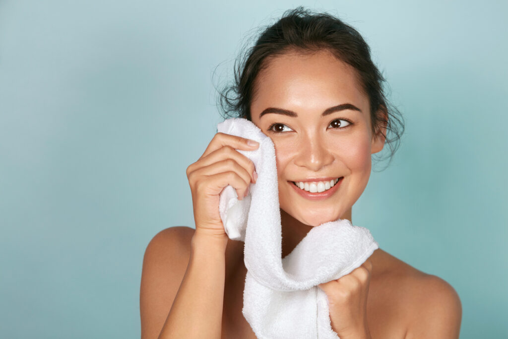 A woman cleaning her face with a white towel