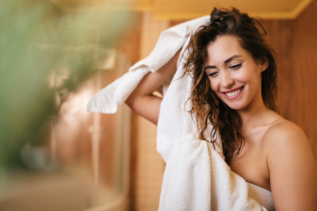 Young beautiful woman using towel and drying her hair in the bathroom.