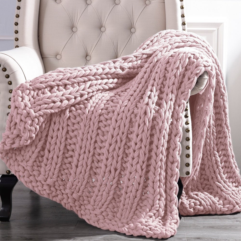 a pink arm woven blanket draped over a white chair
