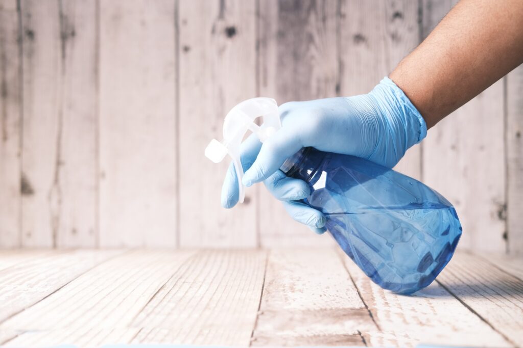 a person in blue gloves spraying a blue spray bottle on a wooden surface