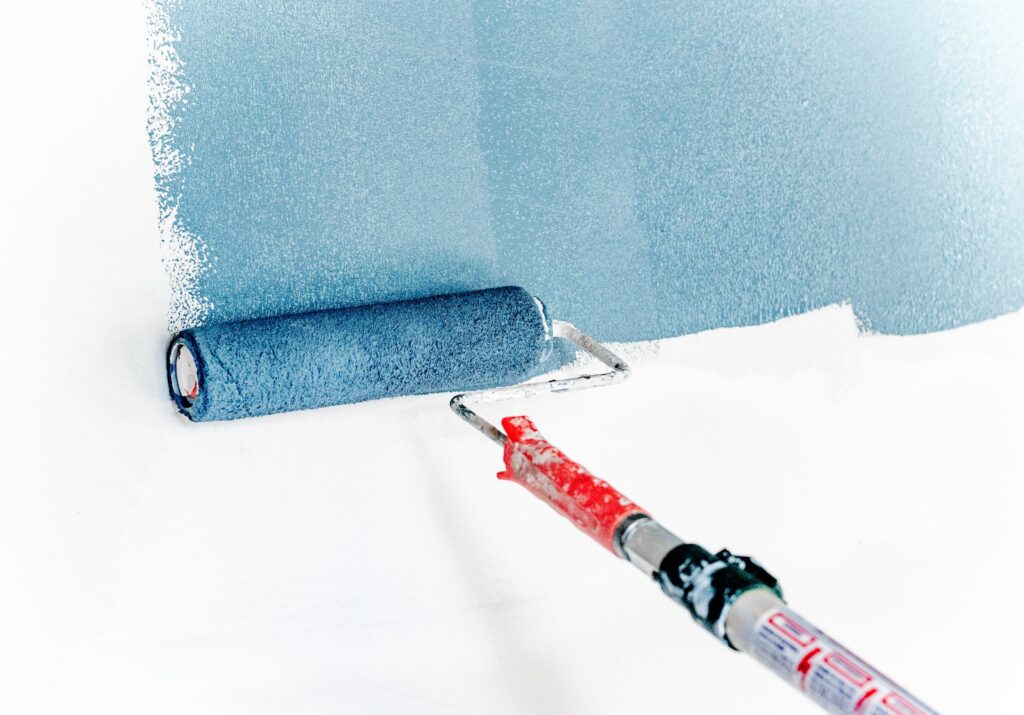 a roller brush with blue paint painting a wall