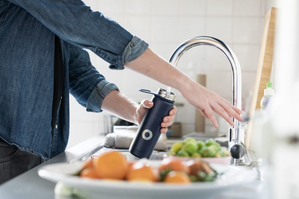 A person in a denim shirt washing a navy blue water water bottle