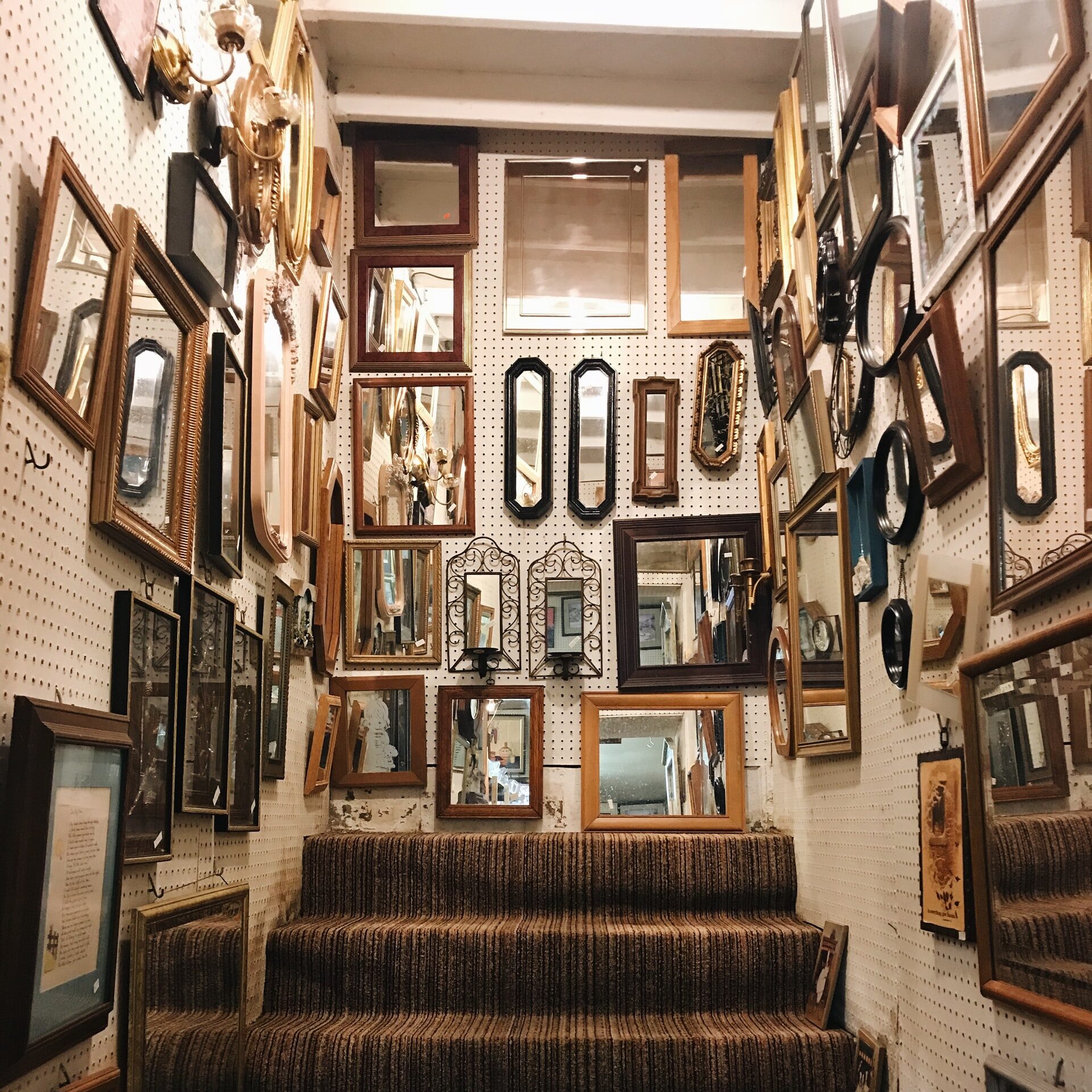 a variety of mirrors and frames hanging in a thrift store