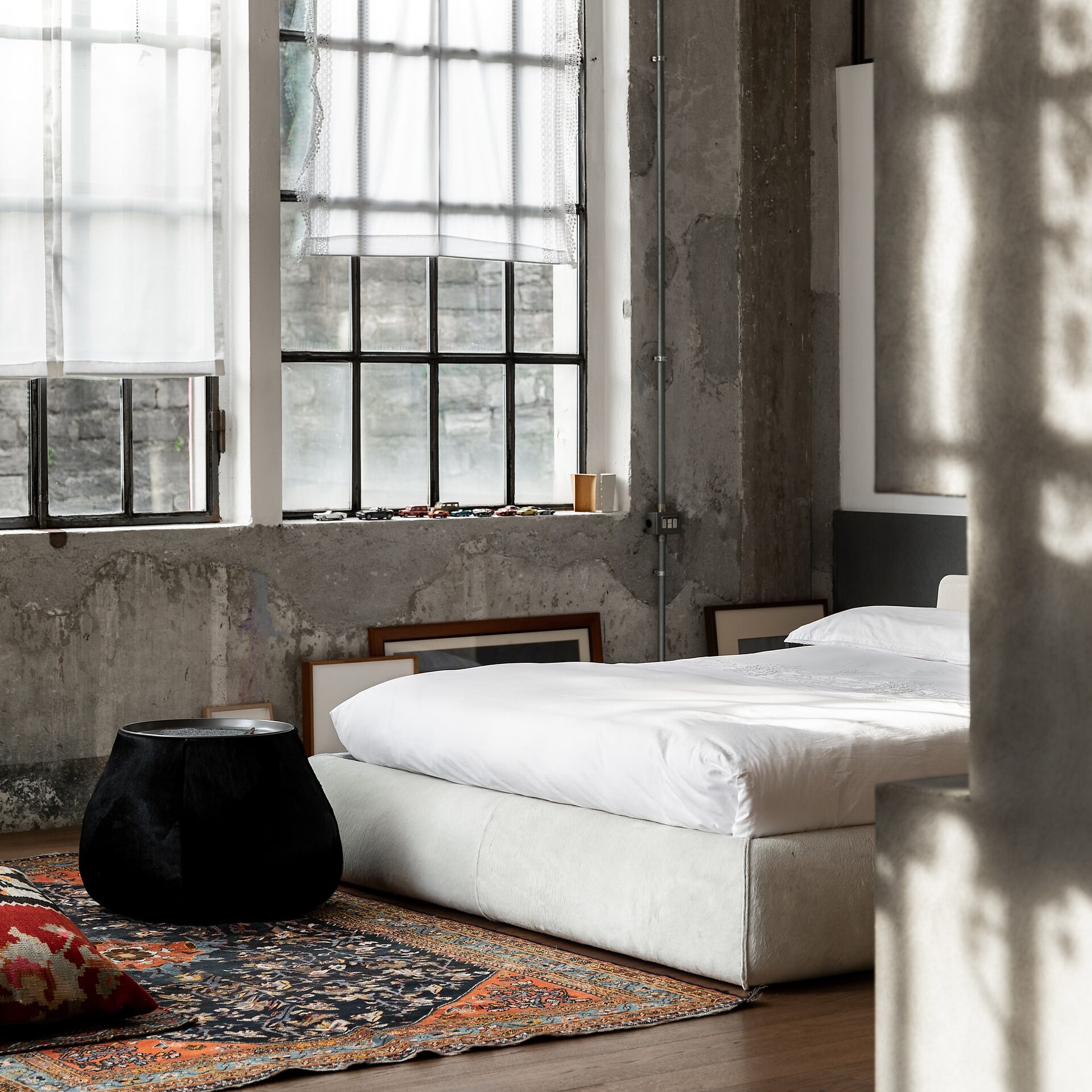 an industrial bedroom with a black stool and white bed