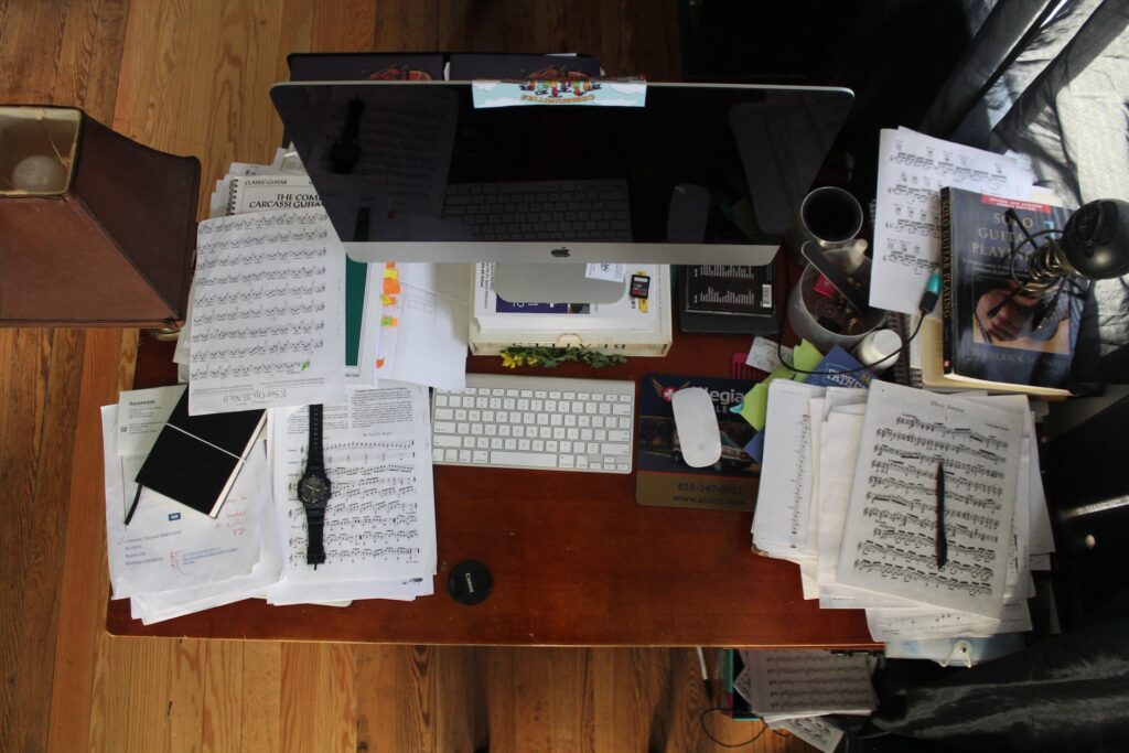 a messy desk area with stacked sheet music and other papers