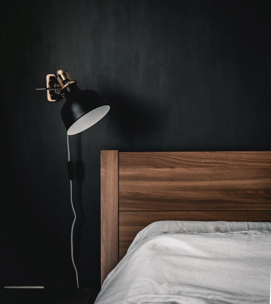 a black bedroom wall with a black lamp and a wooden bed