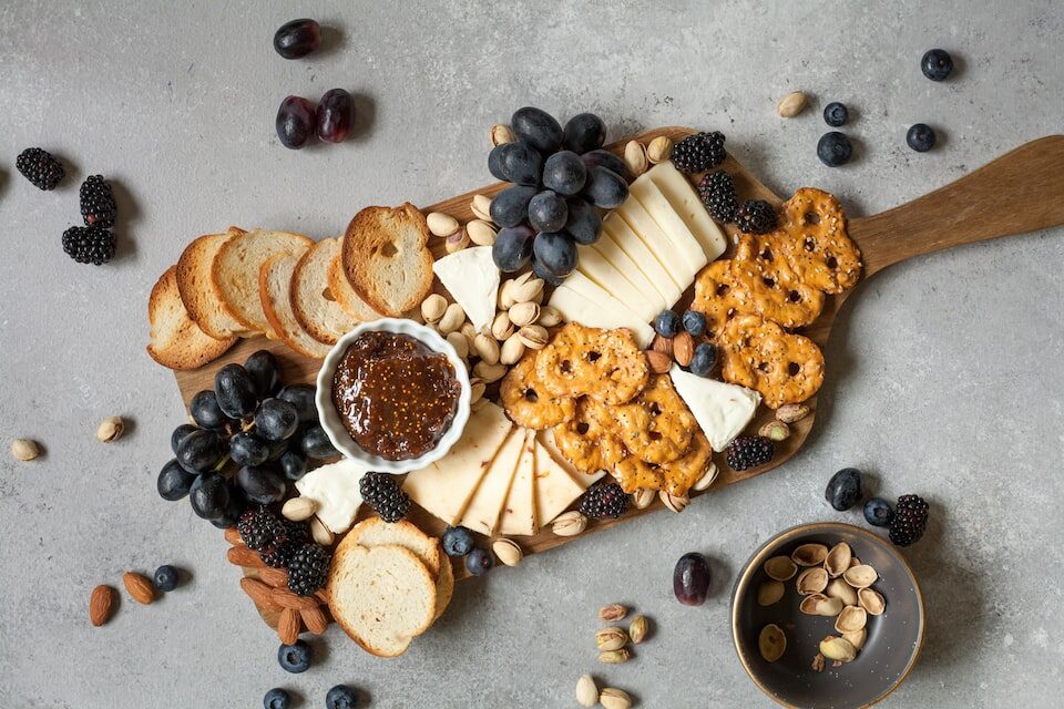 a charcuterie board with pretzels, cheese, and fruit to plan a house party