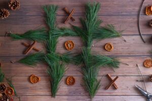 Photo of a tic-tac-toe game with pine needles as the grid. Dried oranges, one of the DIY Christmas ornaments in the article, serve as the O and are winning against the X player.