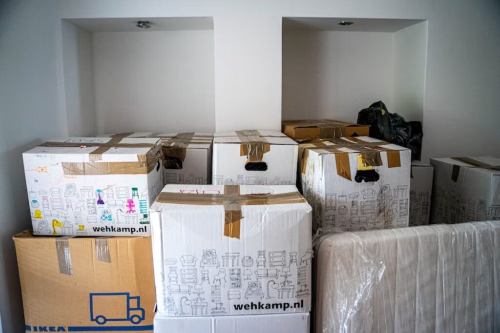 Piles of carboard boxes in a garage. The best housewarming gift ideas will help them deal with the stress of unpacking.
