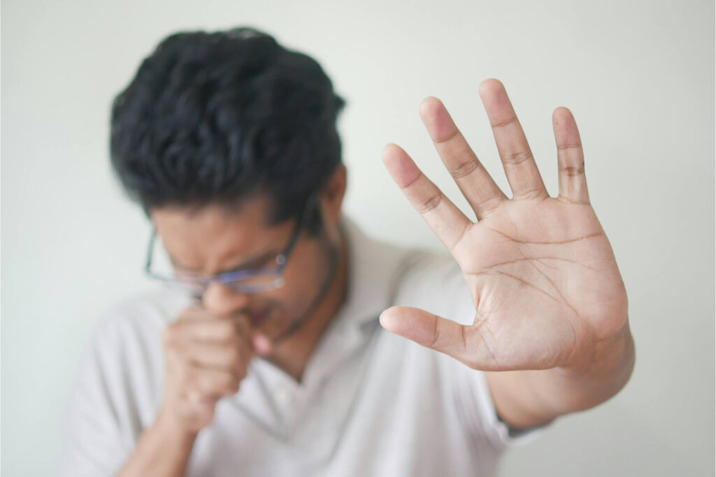 A man doing a stop hand gesture before a sneeze. 