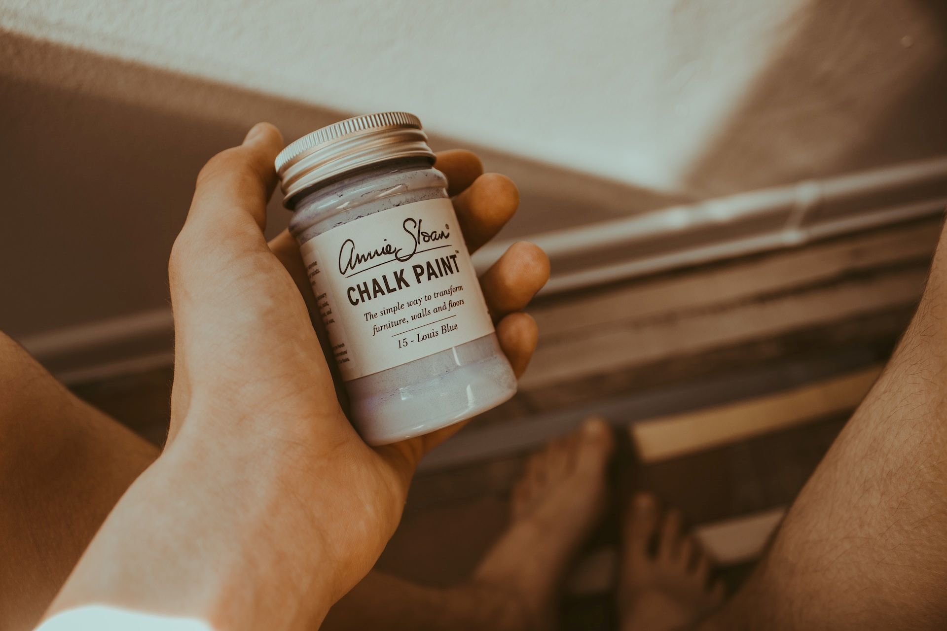 a woman holding a jar of chalk paint learning how to use chalk paint to refinish a picture frame