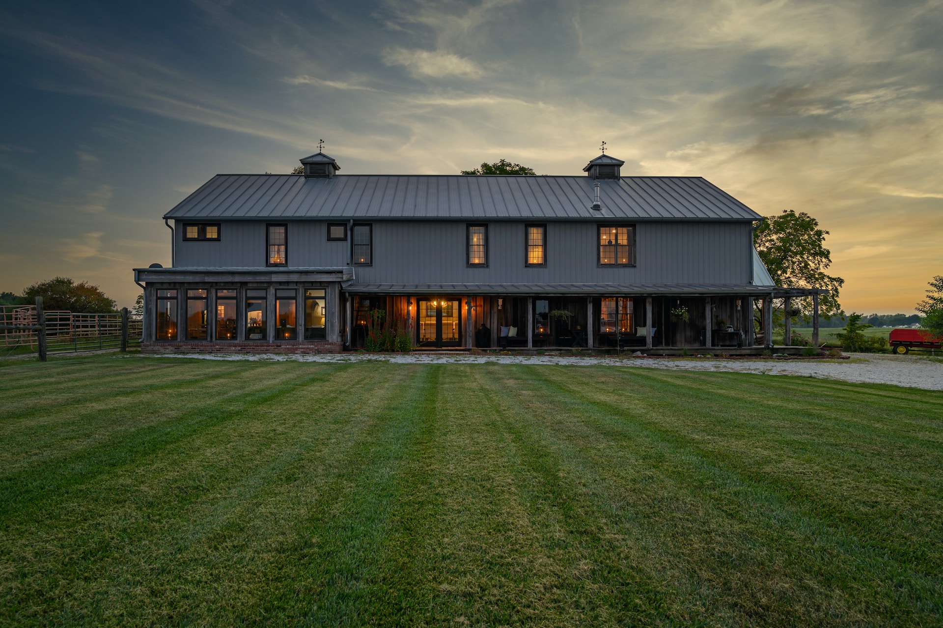 A great example of what a barndominium is. A large grey barn home sitting on lawn with sunset.