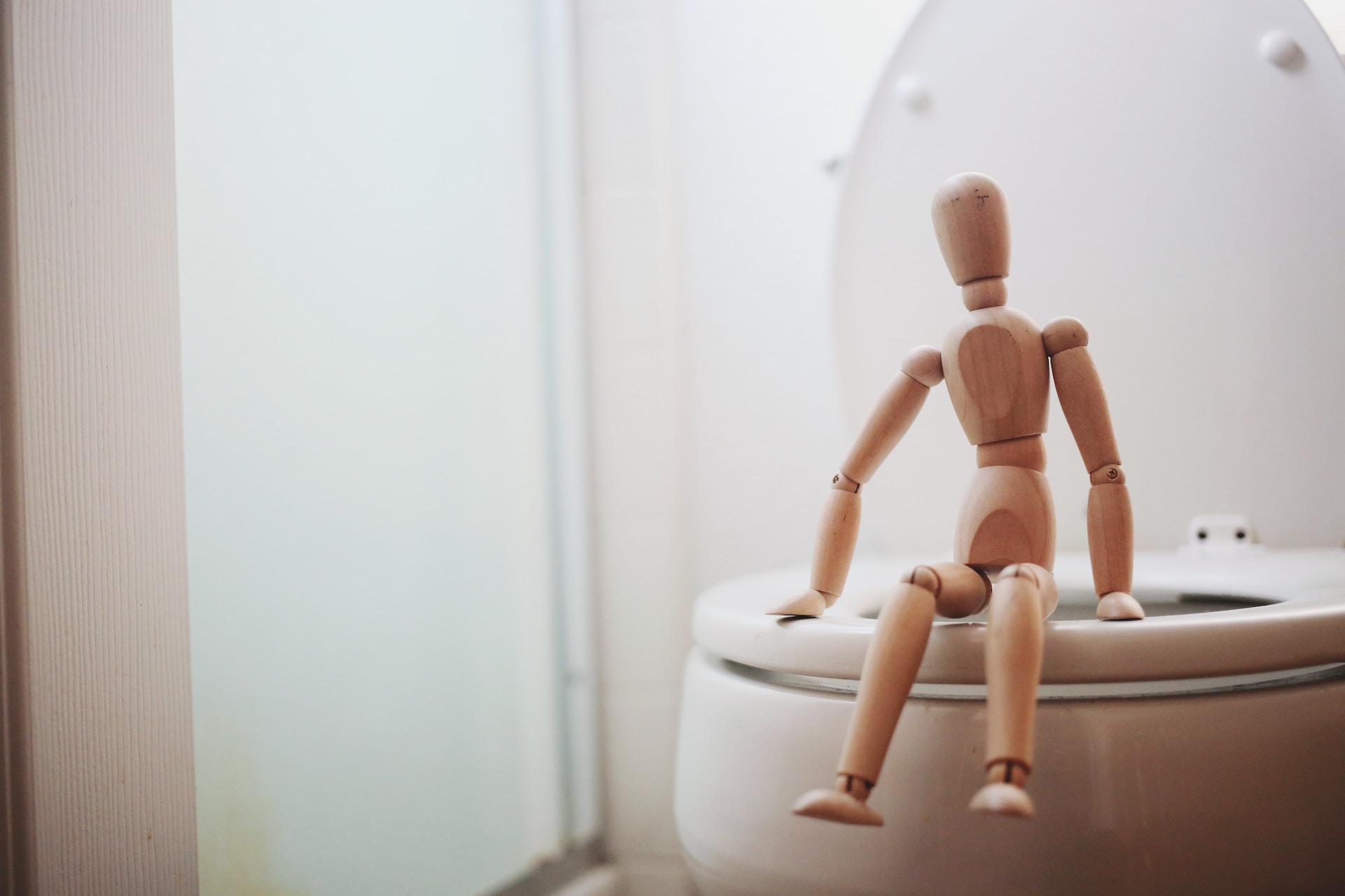 Small wooden figure sitting on edge of toilet.