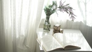 airy drapes behind a decorative table with flowers and a book that are hung by someone who knows how to hang curtains
