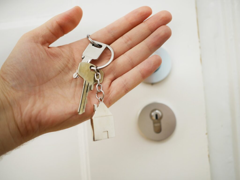 Hands holding house key in front of door.