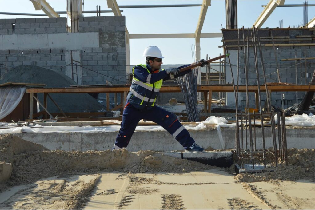 A construction worker bending a steel bar reinforcing concrete