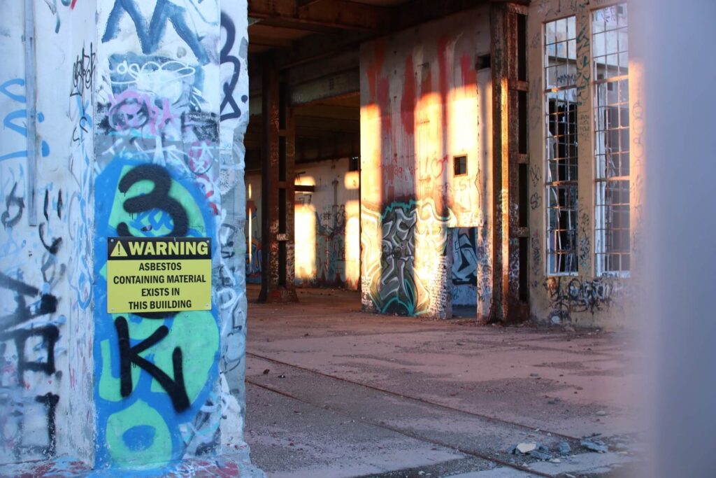 An asbestos warning sign outside an abandoned building.