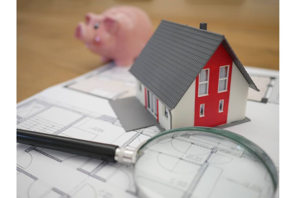 A miniature house, a magnifying glass and a piggy bank.