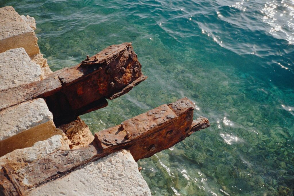 Remnants of beams by the sea covered in rust.
