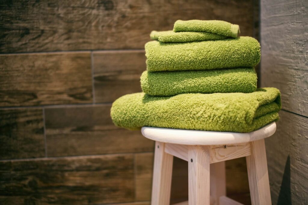 Green towels stacked by size on a stool.