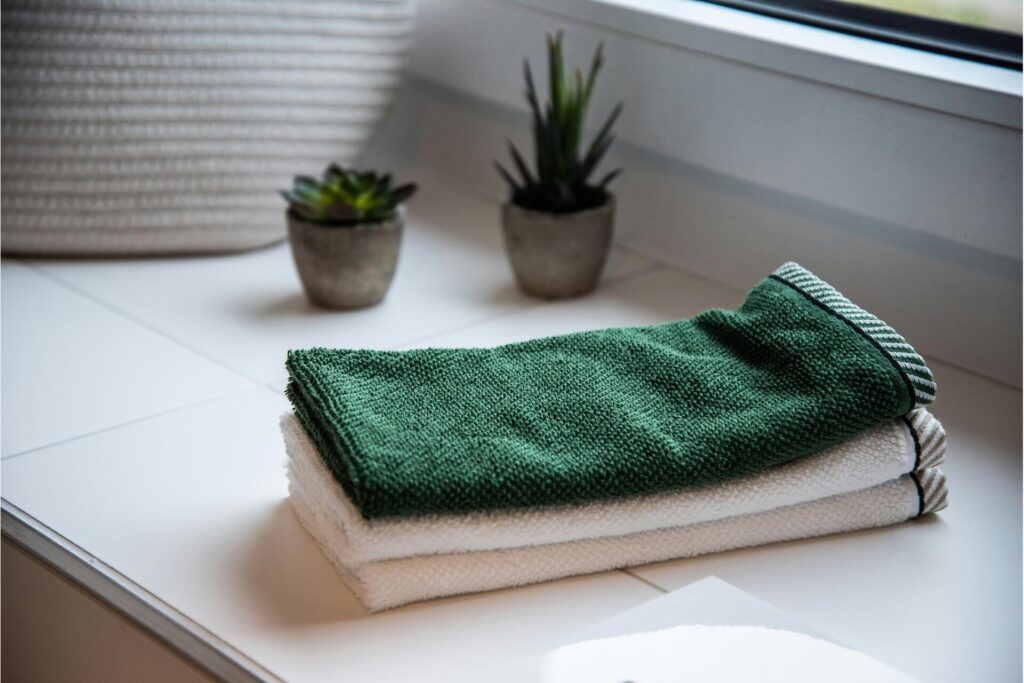 A folded green towel stacked on two folded white ones.