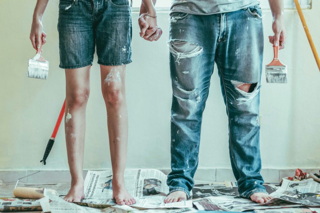 Couple wearing denim stained with white paint and holding paintbrushes 