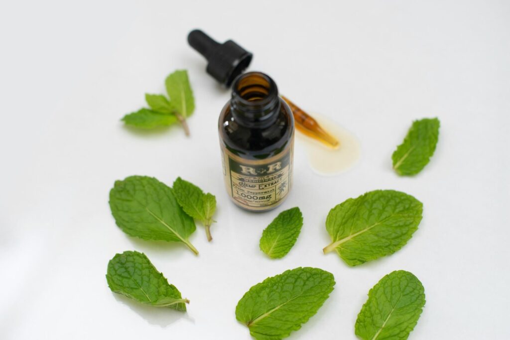 A bottle of peppermint oil surrounded by peppermint leaves