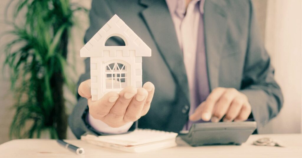 A homeowner holding a replica of a house in their hand and the other hand is on a calculator