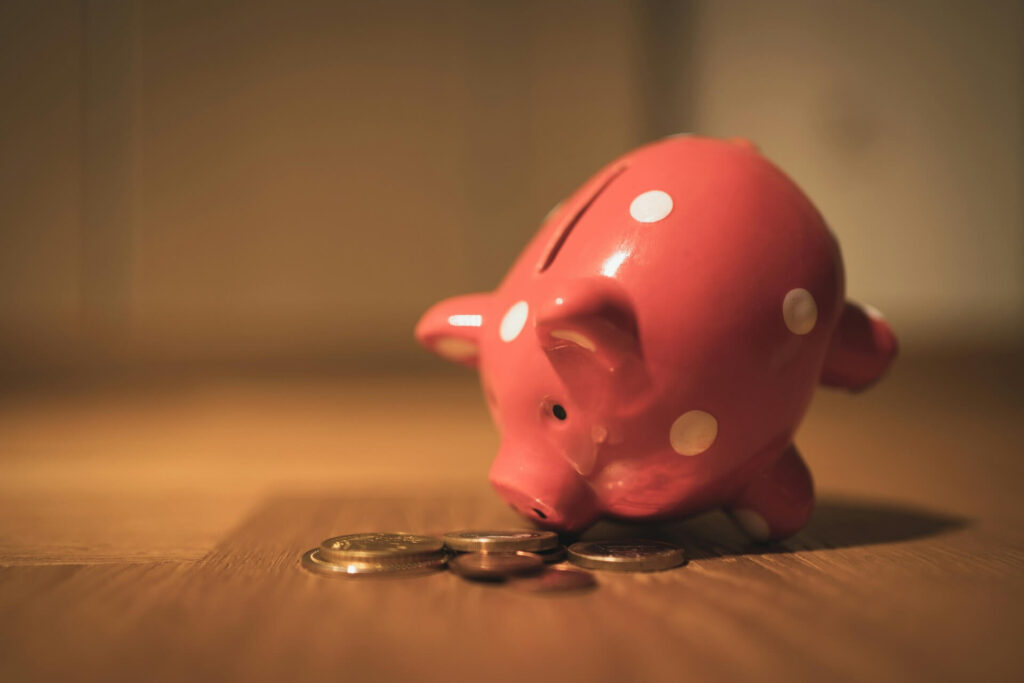 A pink piggy bank with polka dots and coins scattered on the floor.