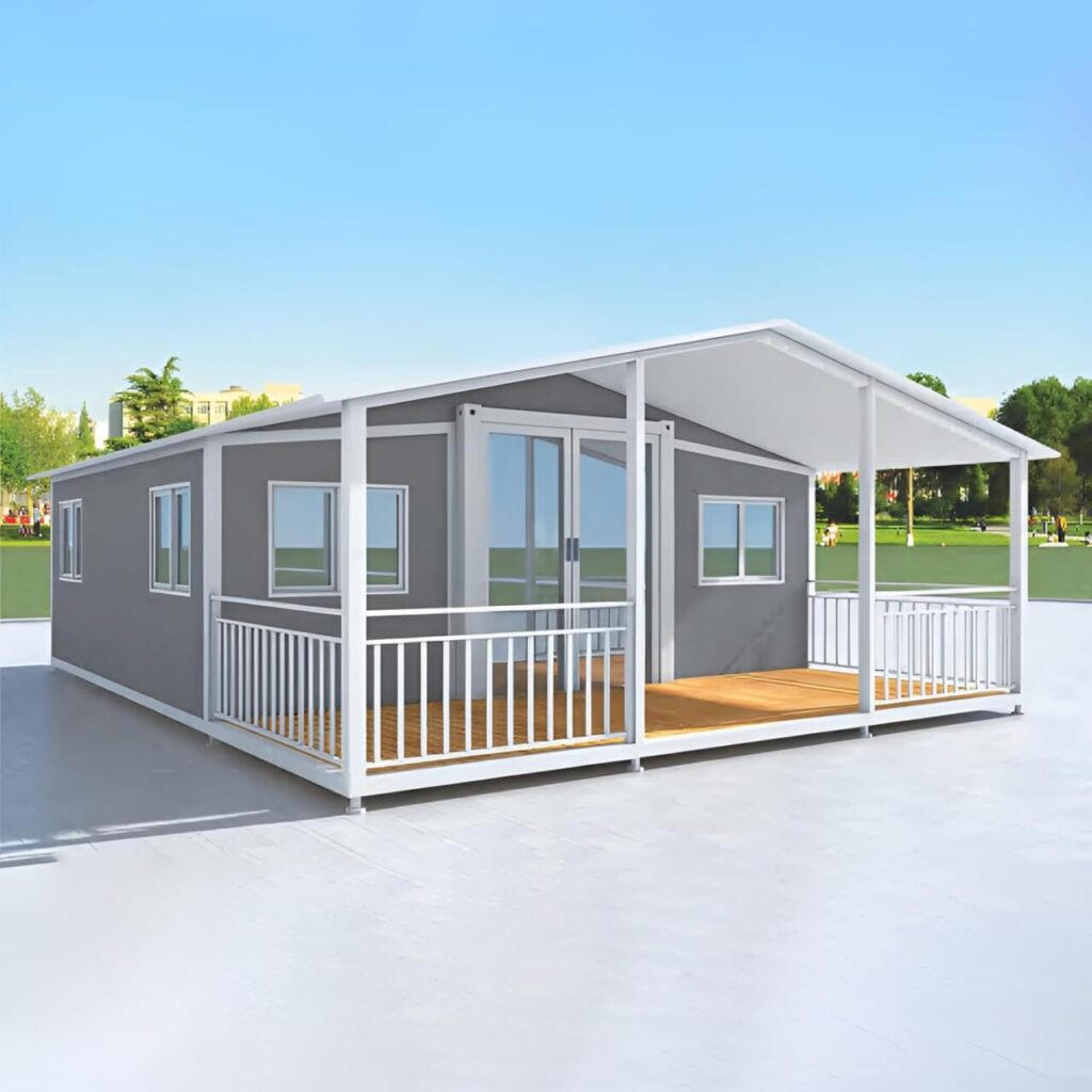 A gray and white rectangular tiny home sits on a concrete slab. It has a wide white front porch with light brown wooden flooring.