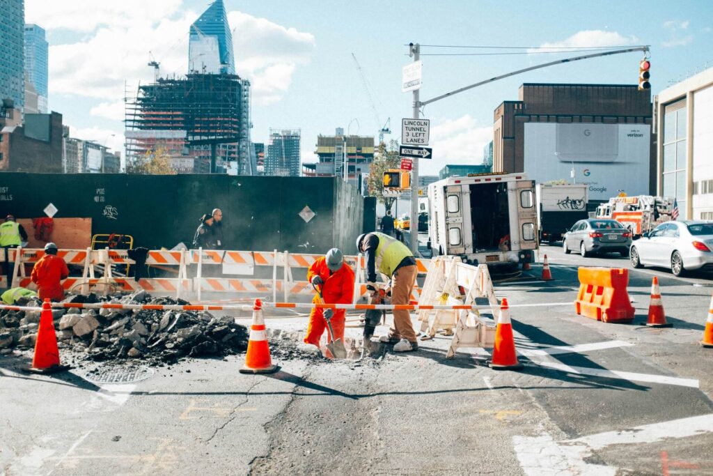 Construction workers excavating a road using a jackhammer and a shovel.