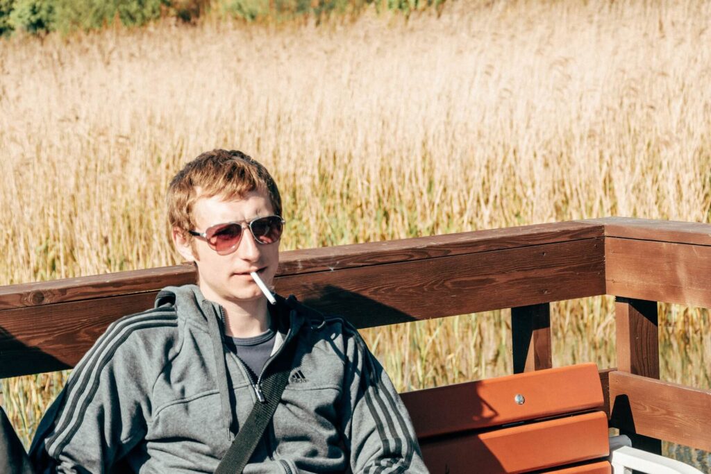 A man smoking at a wooden deck while sitting on a bench.