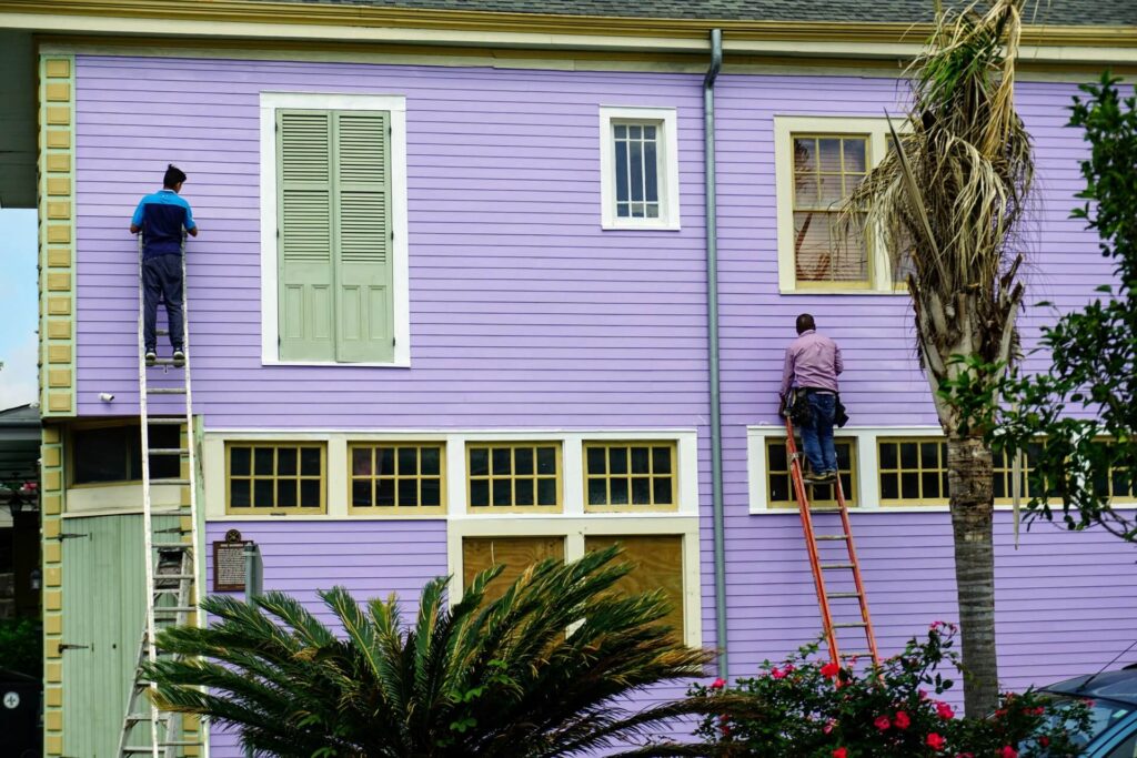 Painters on a ladder applying new vinyl siding colors.