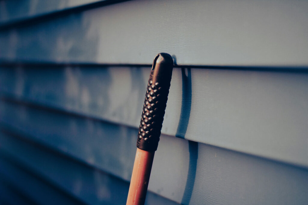 An umbrella handle leaning against aluminum siding panels with slight discoloration.