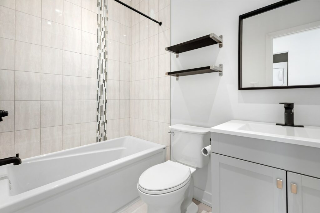 An all-white bathroom gleams without any decorations or countertop belongings. A mirror edged in black sits above the sink.