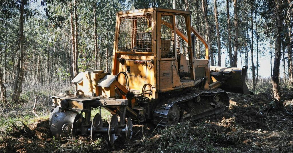 Compact equipment landscaping and clearing a forested area with debris. The small machine has multiple attachments.