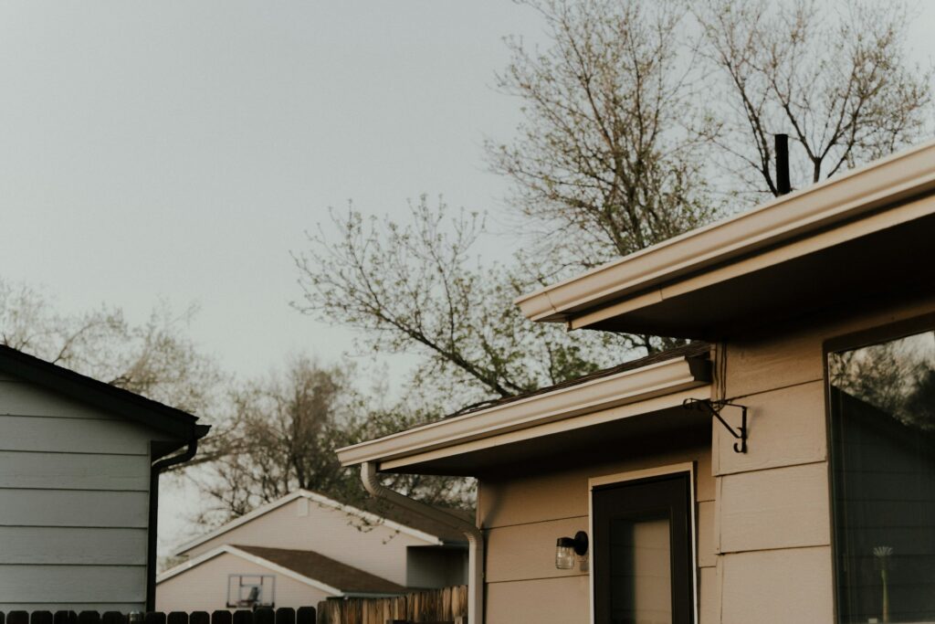 A small tan house sits under a gray sky. Trees with newly budding leaves are in the background.