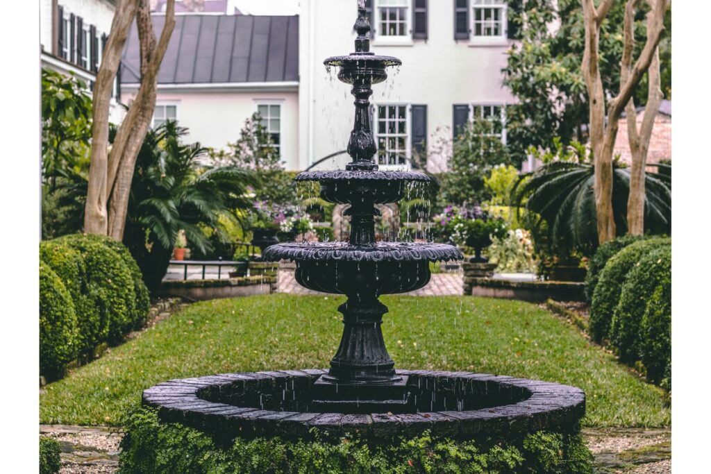 A dark fountain in a vegetated side yard against the backdrop of a white property