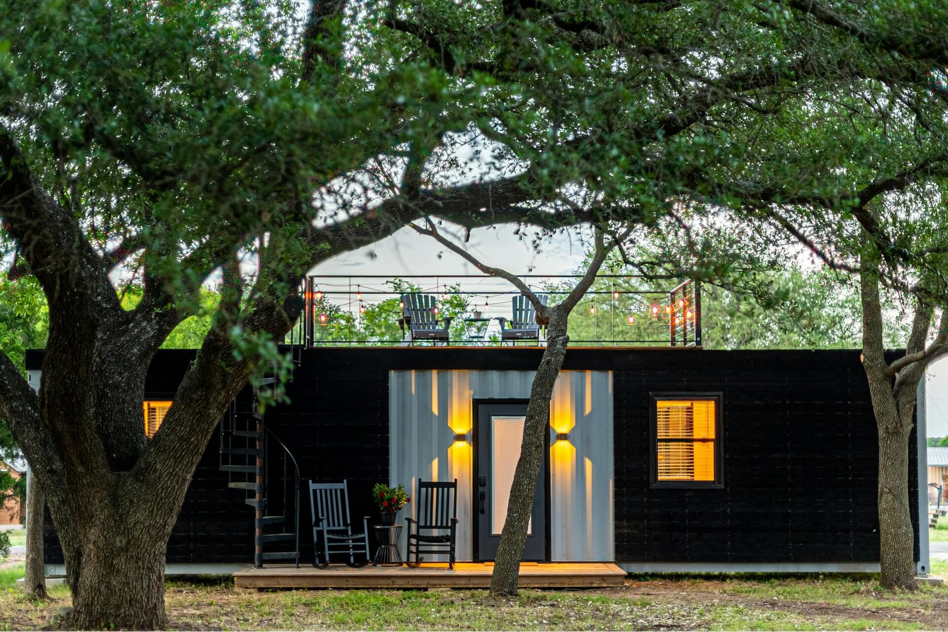 A single-story container home with black exterior surrounded by trees