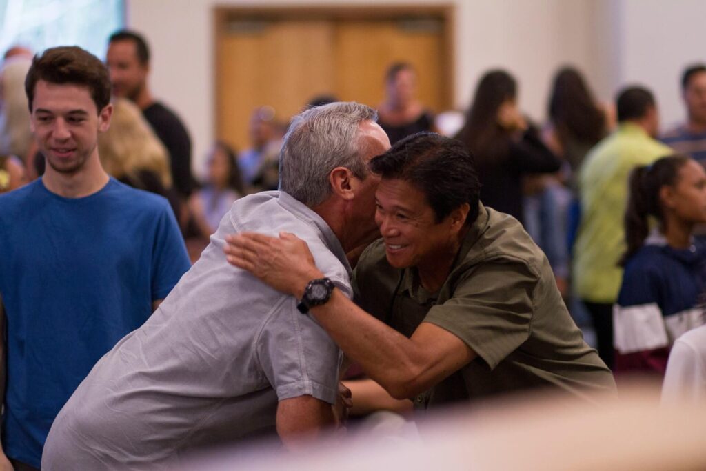 Two adult men hugging each other at a gathering 