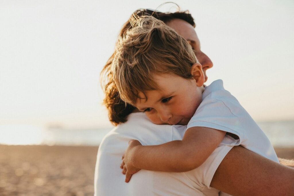 An adult woman and a young boy in white hugging each other