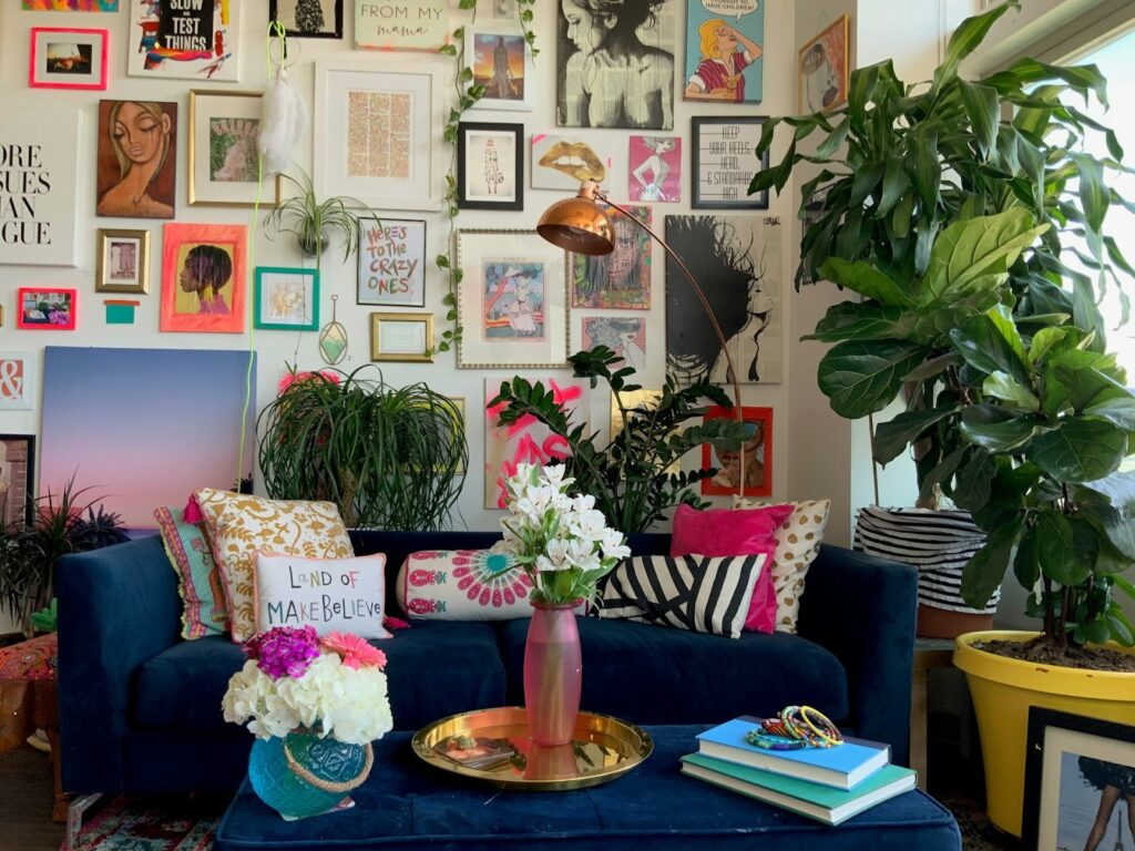 A vibrant living room with a navy blue couch adorned with colorful cushions. Walls are filled with eclectic artwork. Lush plants and flowers add freshness. It embodies and cozy and creative vibe.